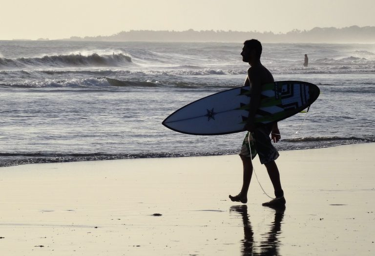 Ein Surfer geht entlang des Strands.