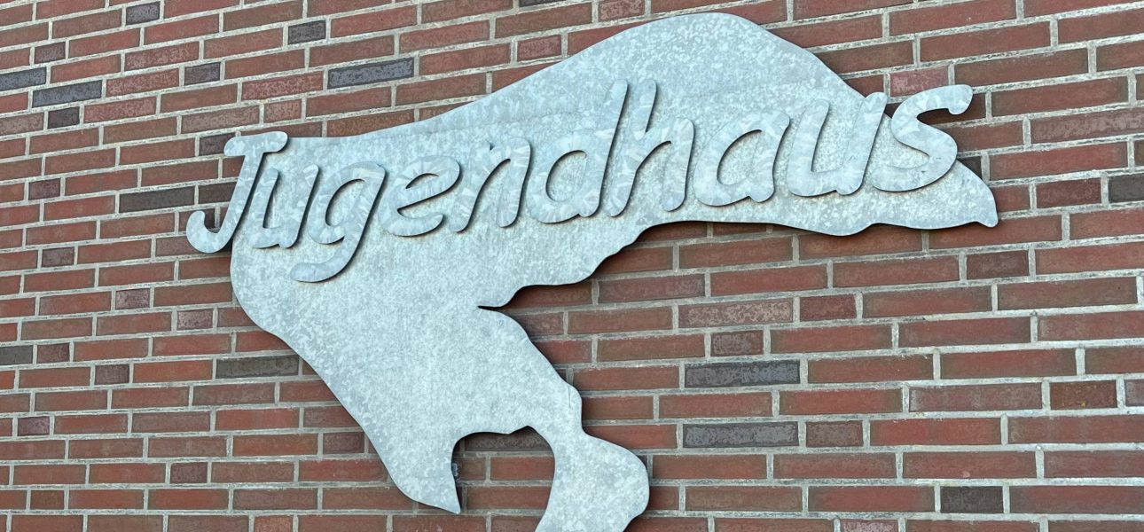 Silbernes Metallschild mit der Aufschrift „Jugendhaus” hängt neben der Eingangstür des Jugendhauses.