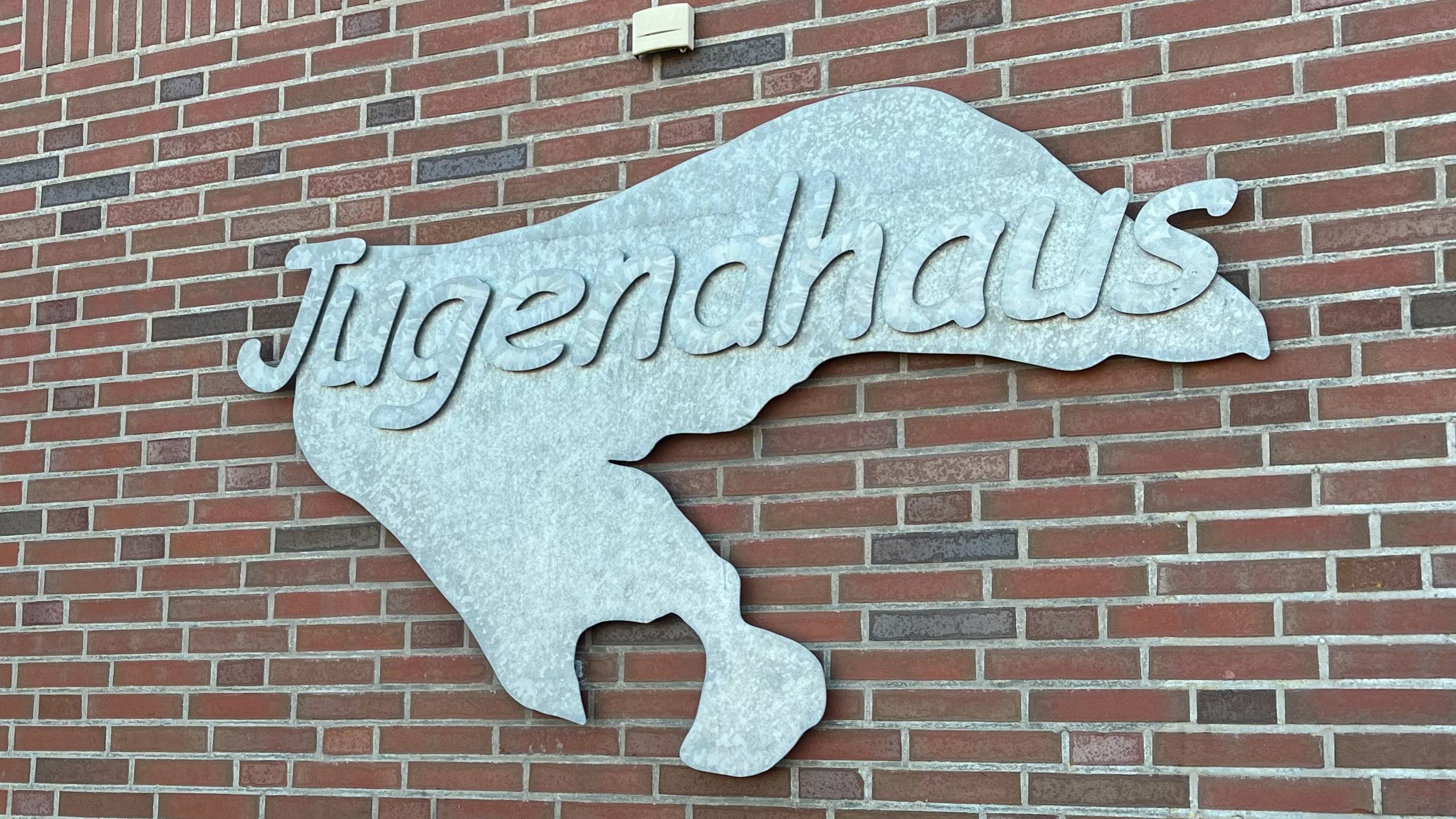 Silbernes Metallschild mit der Aufschrift „Jugendhaus” hängt neben der Eingangstür des Jugendhauses.
