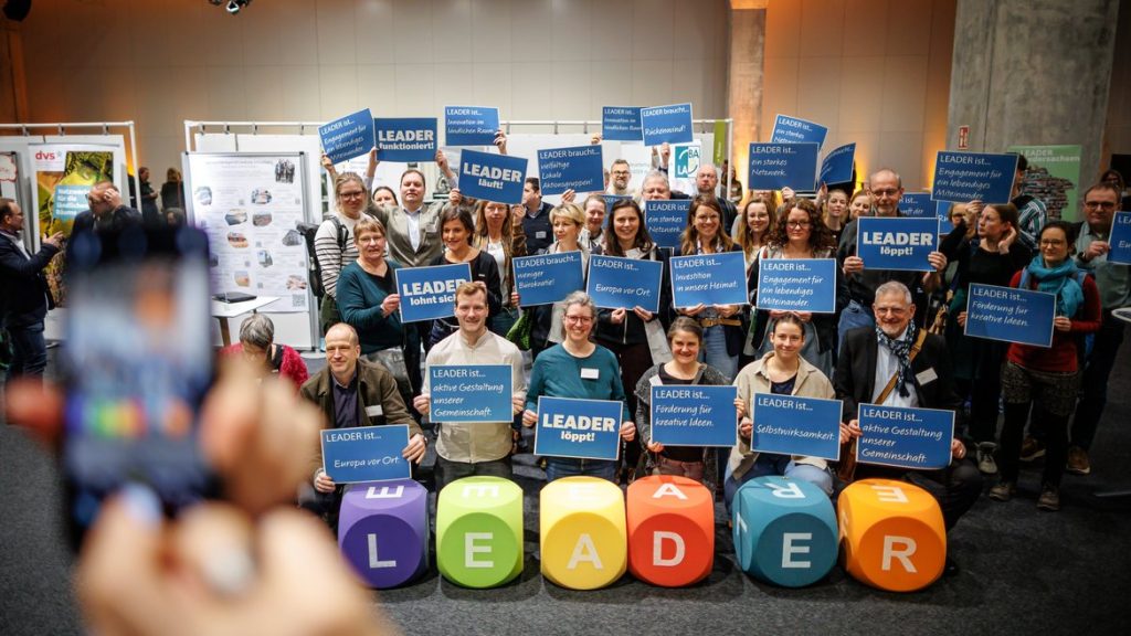 Die Regionalmanager:innen halten Plakate mit Aussagen zur LEADER-Kampagne „LEADER ist ...” LEADER braucht ...” hoch.