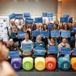 Die Regionalmanager:innen halten Plakate mit Aussagen zur LEADER-Kampagne „LEADER ist ...” LEADER braucht ...” hoch.