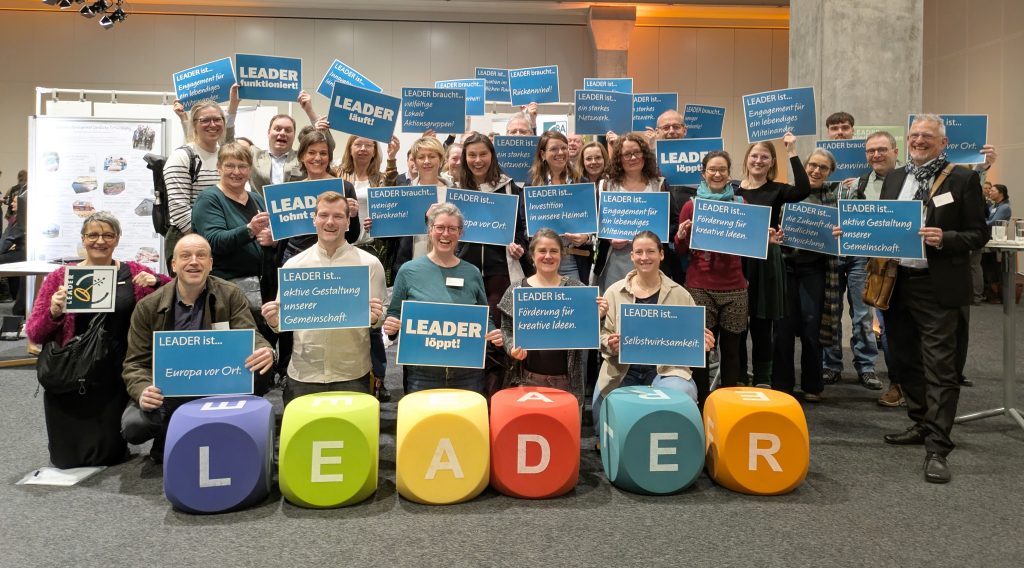 Die Regionalmanager:innen halten Plakate mit Aussagen zur LEADER-Kampagne „LEADER ist ...” LEADER braucht ...” hoch